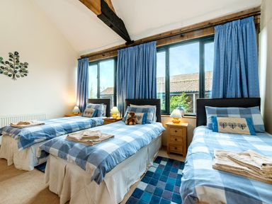 A bedroom with three single beds blue checkered bedding wooden nightstands and blue curtains at Mallard in Wheatacre