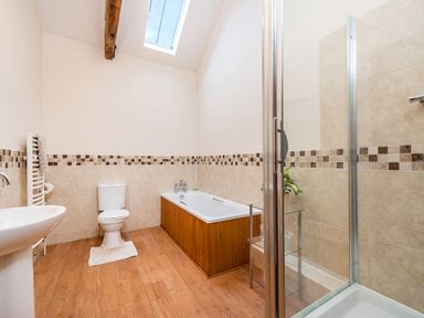 A bathroom with a bathtub wooden panel wood floor toilet white sink and glass shower at Mallard in Wheatacre