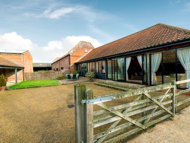 A courtyard with gravel driveway green lawn outdoor table and chairs and a barn style house at Mallard in Wheatacre