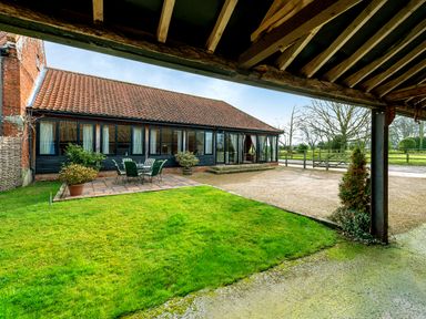 A patio area with outdoor furniture next to a brick and black wooden building with a tiled roof and a grassy lawn at Mallard in Wheatacre