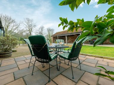 A patio with a table and four chairs with green and white cushions and a bottle with glasses on the table at Mallard in Wheatacre