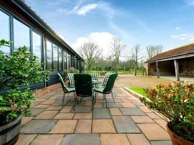 An outdoor patio area with a table and six chairs with green cushions between a building with large windows and a carport at Mallard in Wheatacre
