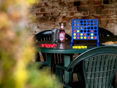A green plastic table with a connect four game set up two glasses a bottle and a plate of snacks in front of a brick wall at Mallard in Wheatacre
