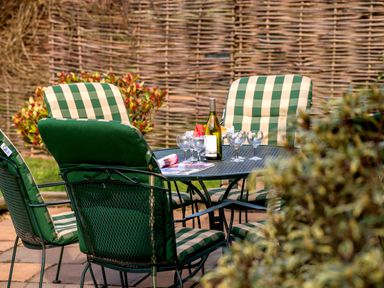 An outdoor patio table with green checkered cushioned chairs a bottle of wine and glasses at Mallard in Wheatacre