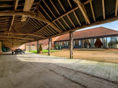 A covered outdoor area with wooden beams and plastic chairs and tables next to a building with large windows and tiled roof at Mallard in Wheatacre