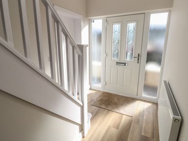A hallway with a white front door a doormat a staircase and a radiator at Wychwood in Hook near Haverfordwest