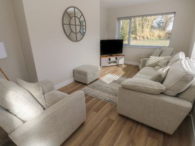 A living room with beige sofas a TV on a stand and a mirror on the wall at Wychwood in Hook near Haverfordwest