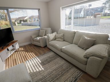 A living room with sofa armchair ottoman television and windows with blinds at Wychwood in Hook near Haverfordwest