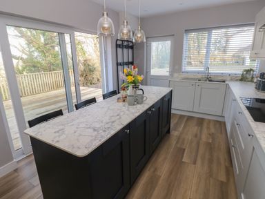 A kitchen with a marble countertop island chairs pendant lights and sliding glass doors at Wychwood in Hook near Haverfordwest