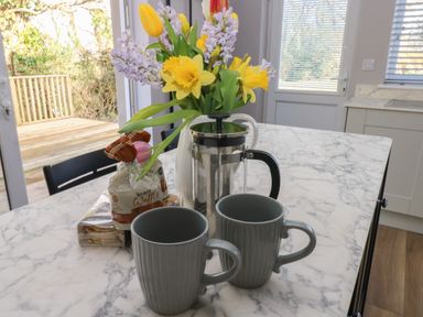 A kitchen table with two gray mugs a french press a vase of spring flowers and packaged waffles at Wychwood in Hook near Haverfordwest