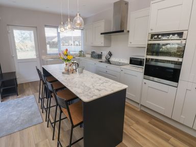 A kitchen with marble countertops bar stools and hanging lights at Wychwood in Hook near Haverfordwest