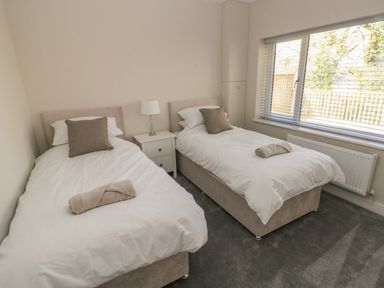 A bedroom with two single beds each with a pillow and rolled towel a nightstand with a lamp and a large window with blinds at Wychwood in Hook near Haverfordwest