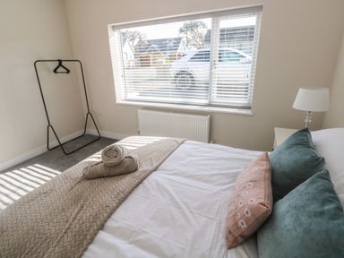 A bedroom with a bed a bedside table with a lamp and a window with blinds at Wychwood in Hook near Haverfordwest