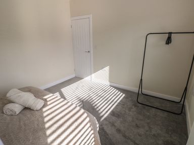 A bedroom with a bed, rolled towels on the bed, a door, and a black clothes rack at Wychwood in Hook near Haverfordwest