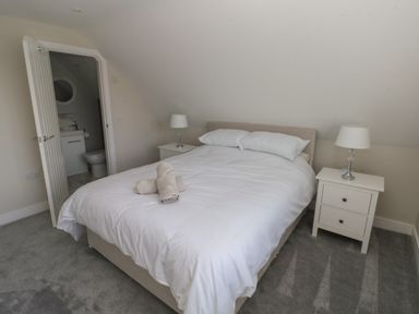 A bedroom with a double bed two bedside tables with lamps an open door to a bathroom at Wychwood in Hook near Haverfordwest
