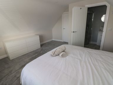 A bedroom with a white dresser towels on a bed and an open door showing a bathroom at Wychwood in Hook near Haverfordwest