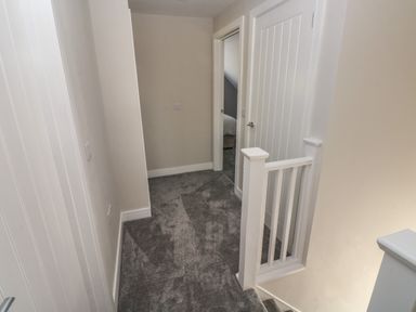 A hallway with gray carpet and white doors near a staircase at Wychwood in Hook near Haverfordwest