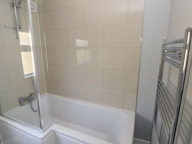 A bathroom with a bathtub shower combination and a chrome towel radiator at Wychwood in Hook near Haverfordwest