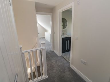 A hallway with carpeted floor leading to a bathroom and a bedroom with a white chest of drawers at Wychwood in Hook near Haverfordwest