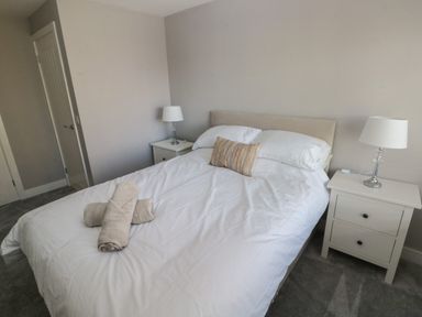 A bedroom with a double bed two bedside tables with lamps and rolled towels on the bed at Wychwood in Hook near Haverfordwest