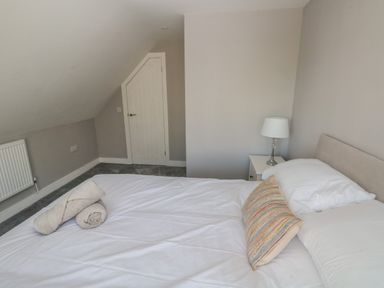 A bedroom with a bed with white linens and a striped pillow a small lamp on a side table and a small door under a sloped ceiling at Wychwood in Hook near Haverfordwest