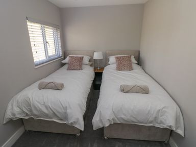 A bedroom with two single beds with white bedding and pillows separated by a bedside table with a lamp at Wychwood in Hook near Haverfordwest