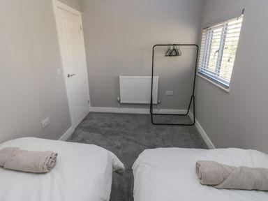 A small bedroom with two beds each with a rolled towel a clothes rack with hangers a radiator and a window with blinds at Wychwood in Hook near Haverfordwest