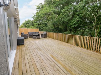 A large wooden deck with outdoor seating and a table surrounded by trees at Wychwood in Hook near Haverfordwest
