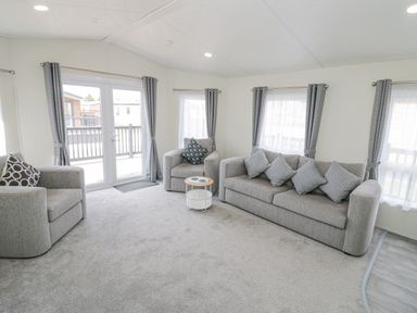 A living room with grey sofas and cushions and a small round table at Long Acres Lodge in Evesham
