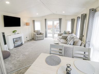 A living room with sofas armchairs a wall-mounted television and a dining table at Long Acres Lodge in Evesham