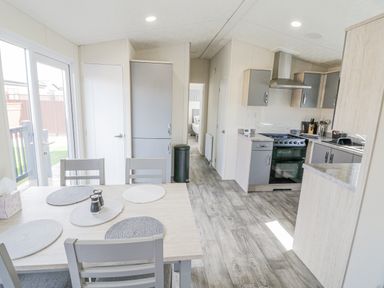 A kitchen and dining area with a wooden table and chairs next to sliding glass doors at Long Acres Lodge in Evesham