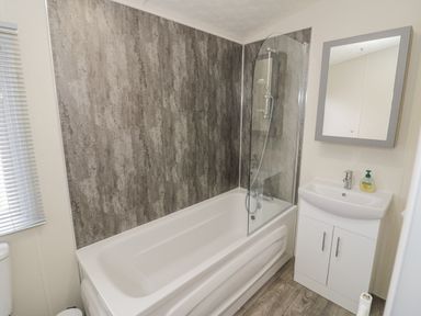 A bathroom with a bathtub shower combination a sink with cabinet and mirror at Long Acres Lodge in Evesham