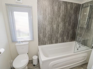 A bathroom with a toilet a bathtub with shower and a window with blinds at Long Acres Lodge in Evesham