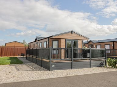 A wooden cabin with a fenced deck area and gravel driveway at Long Acres Lodge in Evesham