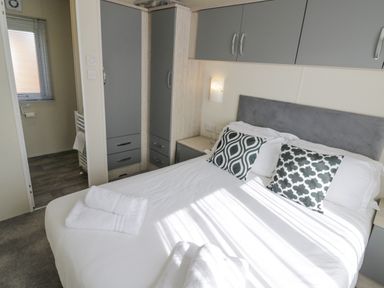 A bedroom with a double bed with patterned pillows towels on the bed and a wardrobe with grey doors at Long Acres Lodge in Evesham