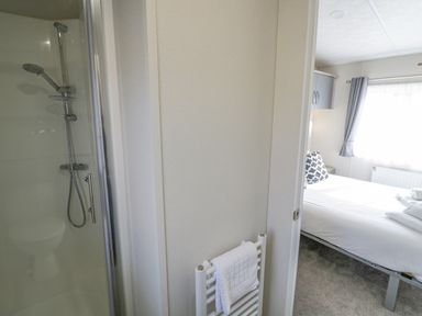 A bedroom with a bed next to a window and a bathroom with a shower visible through an open door at Long Acres Lodge in Evesham