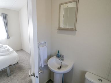 A small bathroom with a pedestal sink towel rack mirror and part of a toilet next to a bedroom with a bed and folded towels at Long Acres Lodge in Evesham