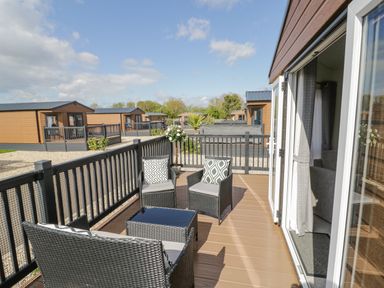A deck with outdoor seating and a table attached to a lodge at Long Acres Lodge in Evesham