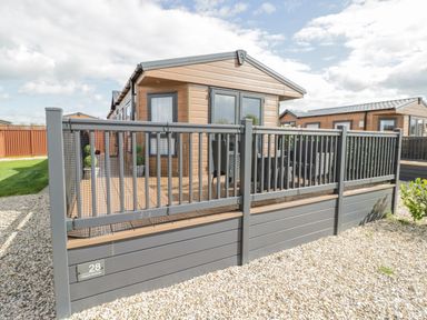 An exterior view of a wooden lodge with a fenced porch area and gravel ground at Long Acres Lodge in Evesham