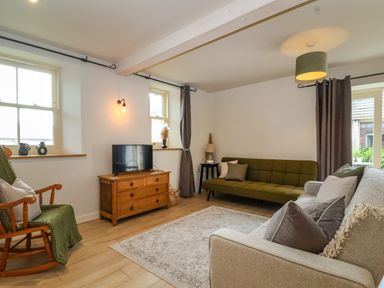 A living room with a green rocking chair a wooden TV stand with a television two sofas and large windows at 8 Rookhaye in Salisbury