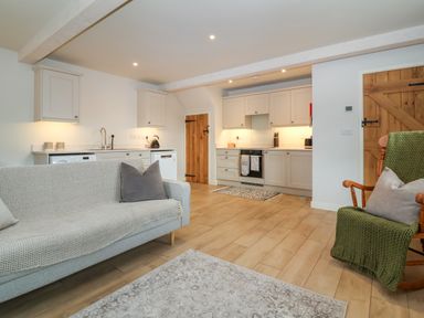 An open plan kitchen and living area with light wood flooring white cabinets and two wooden doors at 8 Rookhaye in Salisbury