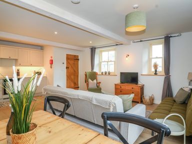 A living room with sofas a wooden cabinet a dining table with chairs and a kitchen area at 8 Rookhaye in Salisbury