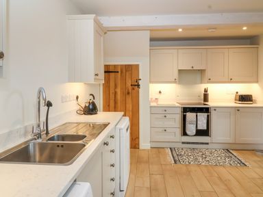 A kitchen with white cabinets a stainless steel sink a black kettle a wooden door and a patterned rug on the floor at 8 Rookhaye in Salisbury
