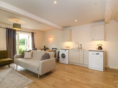 An open plan living area with a grey sofa, green armchair, dining table with chairs, and a kitchen with white cabinets and appliances at 8 Rookhaye in Salisbury