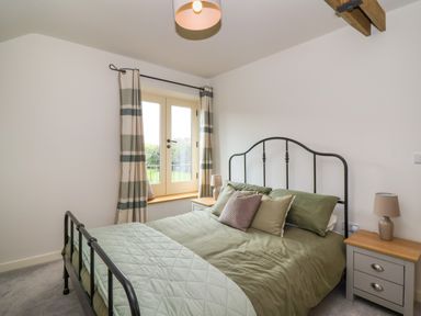 A bedroom with a metal bed frame green bedding two bedside tables with lamps and a window with striped curtains at 8 Rookhaye Salisbury