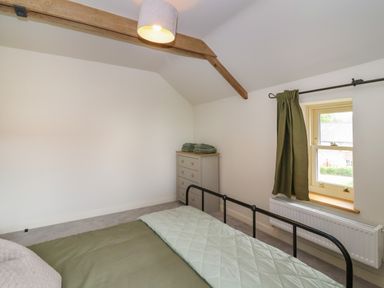 A bedroom with a bed, dresser with towels, a window with curtains, and exposed wooden ceiling beam at 8 Rookhaye Salisbury