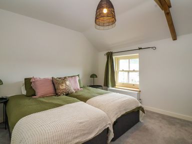 A bedroom with two beds covered in green and white bedding pink and floral cushions bedside tables with green lamps and a window with green curtains at 8 Rookhaye in Salisbury