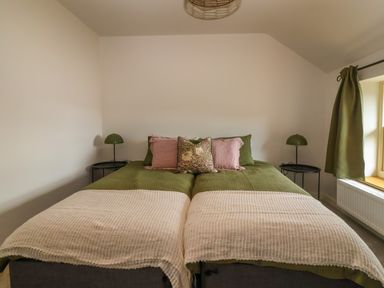 A bedroom with two single beds pushed together with green bedding and pink pillows with matching green lamps on round black bedside tables at 8 Rookhaye Salisbury