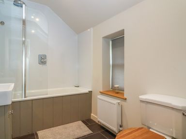 A bathroom with a bathtub shower combination a toilet with wooden seat a small window with a blind and a radiator below at 8 Rookhaye in Salisbury