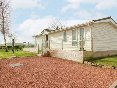 A white mobile home with glass railings on a wooden deck surrounded by lawn and red gravel at Plot 32 in High Hesket near Armathwaite